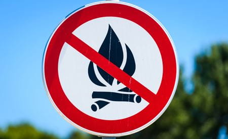 A no campfire sign with a red slash over a campfire icon against a blue sky.