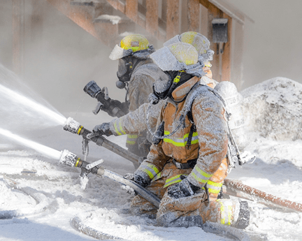 Two firefighters in protective gear kneeling and spraying foam during a training exercise.